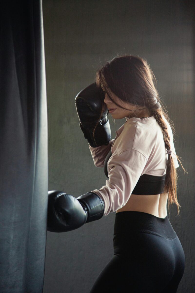 Woman practicing boxing with gloves in an indoor gym setting, focusing on strength and fitness.